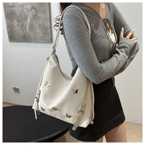 Vue détaillée du sac hobo crème avec rivets papillon et bandoulière réglable en gros plan