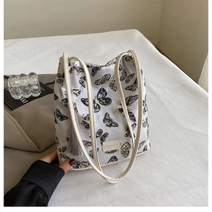 Vue détaillée de la broderie papillon et du pompon sur le sac seau gris clair