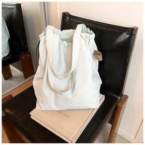 Detail of mint green nylon tote bag featuring drawstring closure and side leather tag