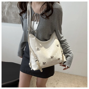 Détail du sac hobo crème avec charms papillon argentés et texture en cuir brillant
