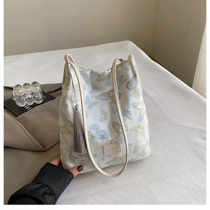 Gros plan du sac fourre-tout en jacquard beige avec broderies papillon et glands en soie