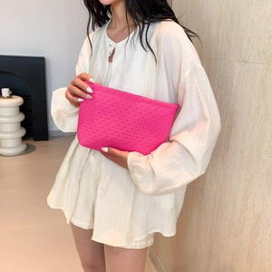 Chic rose pink woven envelope clutch bag held by model wearing a white shirt