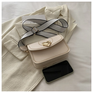 Chic beige crossbody bag with heart buckle compared to a smartphone for size reference