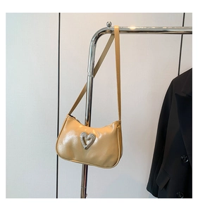 Detail of beige faux leather underarm bag featuring a large heart-shaped rhinestone buckle