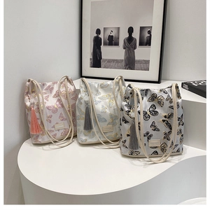 Vue détaillée de trois sacs seaux en satin avec broderie papillon et pompons