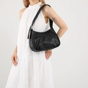 Minimalist black pleated faux leather shoulder bag with wide strap on a white dress model