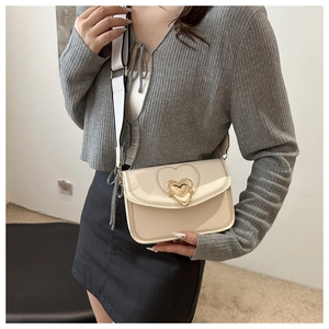 Close-up of cream crossbody bag with golden heart clasp and decorative short chain