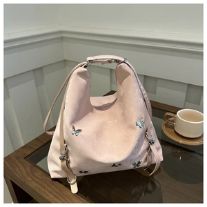 Détail du sac hobo en velours rose avec charms papillon argentés sur surface en bois
