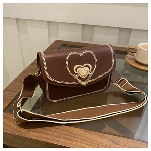 Detail of embroidered heart and metal magnetic buckle on brown leather crossbody bag