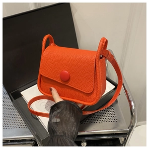 Detail der orangefarbenen Umhängetasche aus Leder mit Narbung und großer runder Schnalle