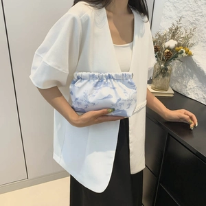 Elegant woman in white blazer holding a light blue printed cloud bag in a home setting