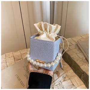 Detail of blue woven box bag with faux pearl handle and gold chain on art books