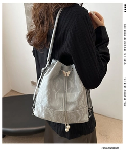 Détail du sac seau gris clair avec texture plissée et pendentif papillon élégant