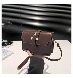 Detailed view of dark brown glossy shoulder bag with gold hardware and zipper accent
