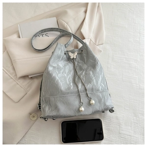 Détail du sac seau gris clair avec texture froissée, boucle papillon et perles blanches