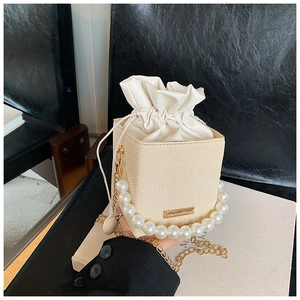 Detail of straw woven box bag featuring white pearl handle and gold chain strap