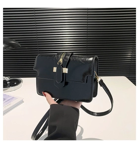 Detail of black patent leather crossbody bag with elegant gold T-bar buckle closure