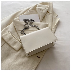 Detail of a minimalist cream-white rectangular crossbody bag with silver chain strap