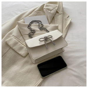 Detail of cream mini crossbody bag featuring a rhinestone bow and silver chain strap