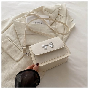 Détail du sac à bandoulière blanc crème avec boucle papillon argentée sur beige