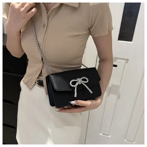 Detail of black leather crossbody bag with sparkling silver rhinestone bow and chain strap