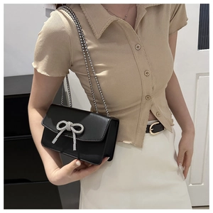 Detail of black leather handbag featuring a sparkling rhinestone bow and silver chain strap