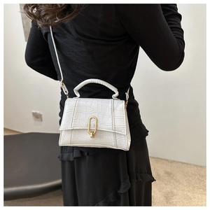 Detail of white crocodile embossed texture and gold oval twist lock on a shoulder bag