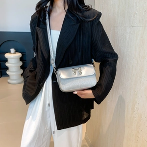 Silberne Glitzer-Umhängetasche mit Metallschleife, am Modell im minimalistischen Stil