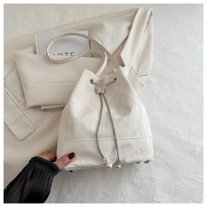Détail du sac seau blanc avec texture craquelée, boucle papillon et breloque en perles