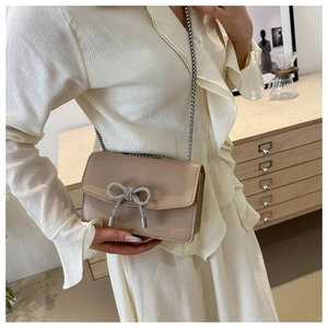 Detail of beige PU leather shoulder bag featuring a sparkling rhinestone bow and silver chain