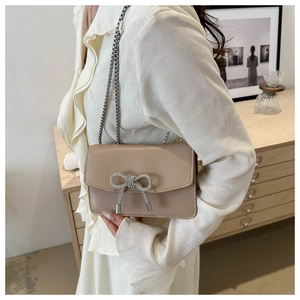 Detail of light apricot chain shoulder bag featuring a sparkling rhinestone bow buckle
