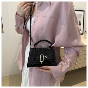Detail of black faux crocodile leather handbag with gold U-shaped lock shown on a model