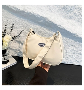 Detail of cream hobo bag showing the SHILAIEN logo plaque and smooth nylon fabric