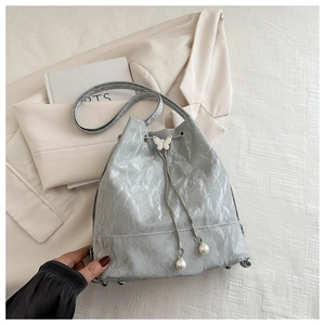 Détail du sac seau argenté avec texture plissée, papillon argenté et cordon en perles