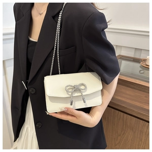 Close-up of white crossbody bag with rhinestone bow and silver chain on black blazer