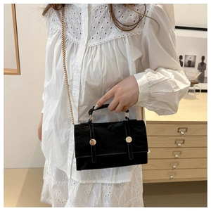 Detail of black crossbody bag with gold chain strap shown on white lace shirt outfit
