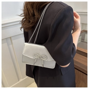 Close-up of a silver metallic crossbody bag featuring a sparkling rhinestone bow detail