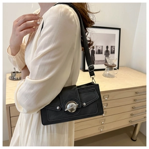 Detail of black suede shoulder bag with unique silver planet buckle worn by model