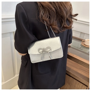 Silver glitter crossbody bag with rhinestone bow detail shown on black blazer shoulder