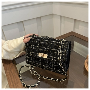 Détail de la texture en tweed noir et doré avec fermoir rotatif en métal et bandoulière chaîne