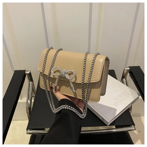 Detailed shot of beige faux leather handbag with sparkling rhinestone bow and silver chain