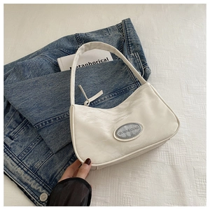 Detail of white pleated crescent bag with silver oval logo plate and glossy finish