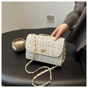 Gros plan sur la texture en tweed beige avec fil doré et fermoir rotatif de ce sac