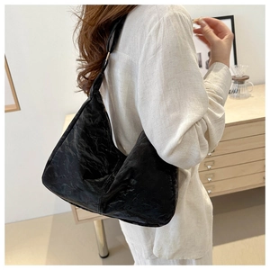 Detail shot of a black pleated hobo shoulder bag worn by a model in a minimalist setting