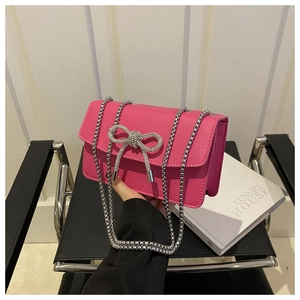 Detail of bright pink leather crossbody bag with silver rhinestone bow and chain strap