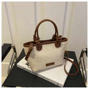 Detail of hand-woven straw tote bag with brown leather handles and knot decorative accents