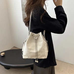 Sac seau crème avec chaîne, détail papillon en métal et cordons en perles sur modèle