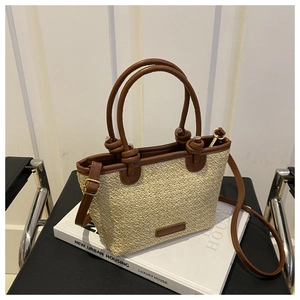 Detail of straw tote bag showing woven texture, brown leather handle and metal hardware