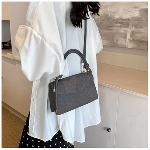 Detailed view of grey textured crossbody bag with gold hardware on a model