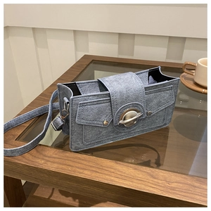 Detail of light blue denim shoulder bag featuring a unique planet-shaped metal buckle